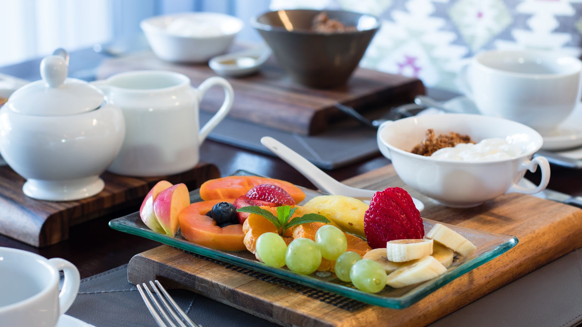 Een ontbijtsetting met een fruitplateau, koffiekopjes en een theepot.
