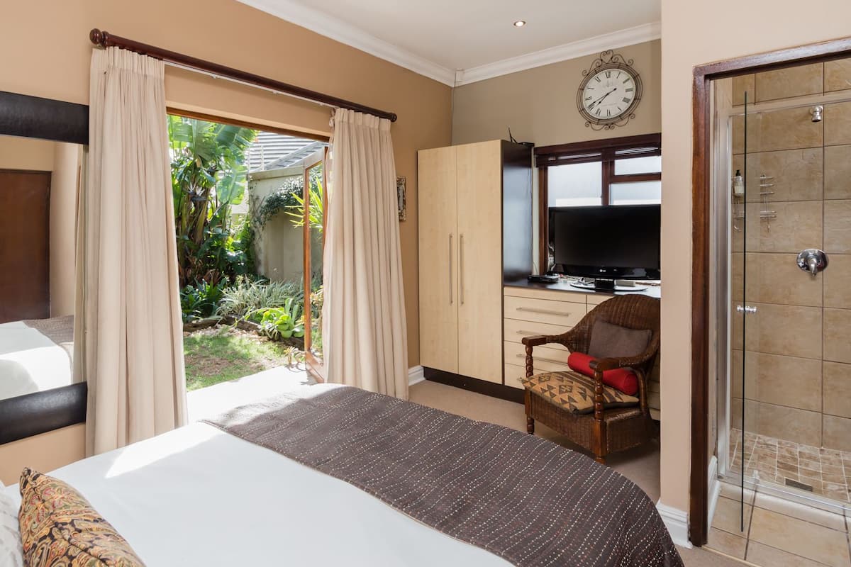 Quarto de hotel com uma cama grande, televisão, guarda-roupa e porta de vidro para um jardim.