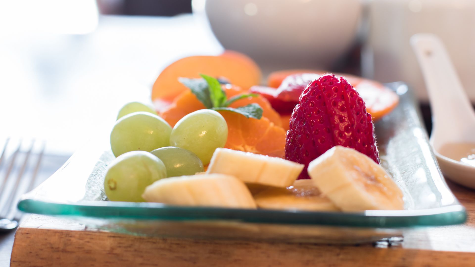 Une assiette de fruits comprenant des raisins, des bananes, des fraises et une orange, le tout présenté sur une assiette en verre.
