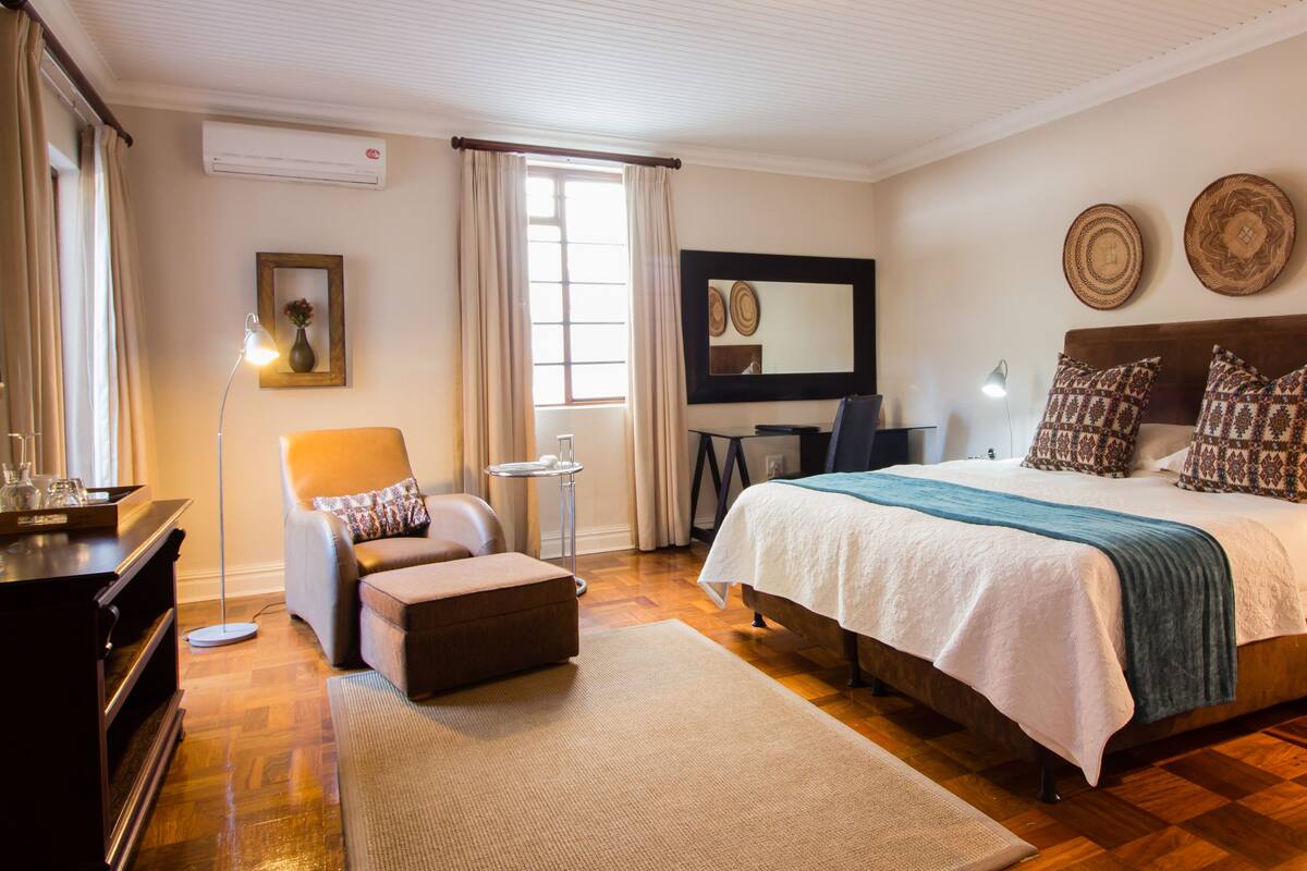 Quarto com uma cama grande, uma escrivaninha, uma cadeira e uma mesa pequena.