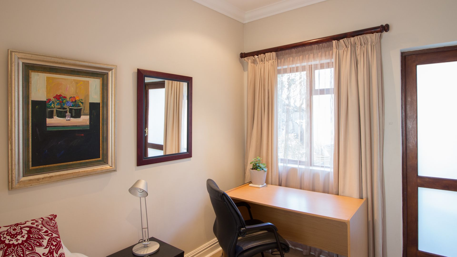 A room with a desk, chair, lamp, and two windows with curtains.