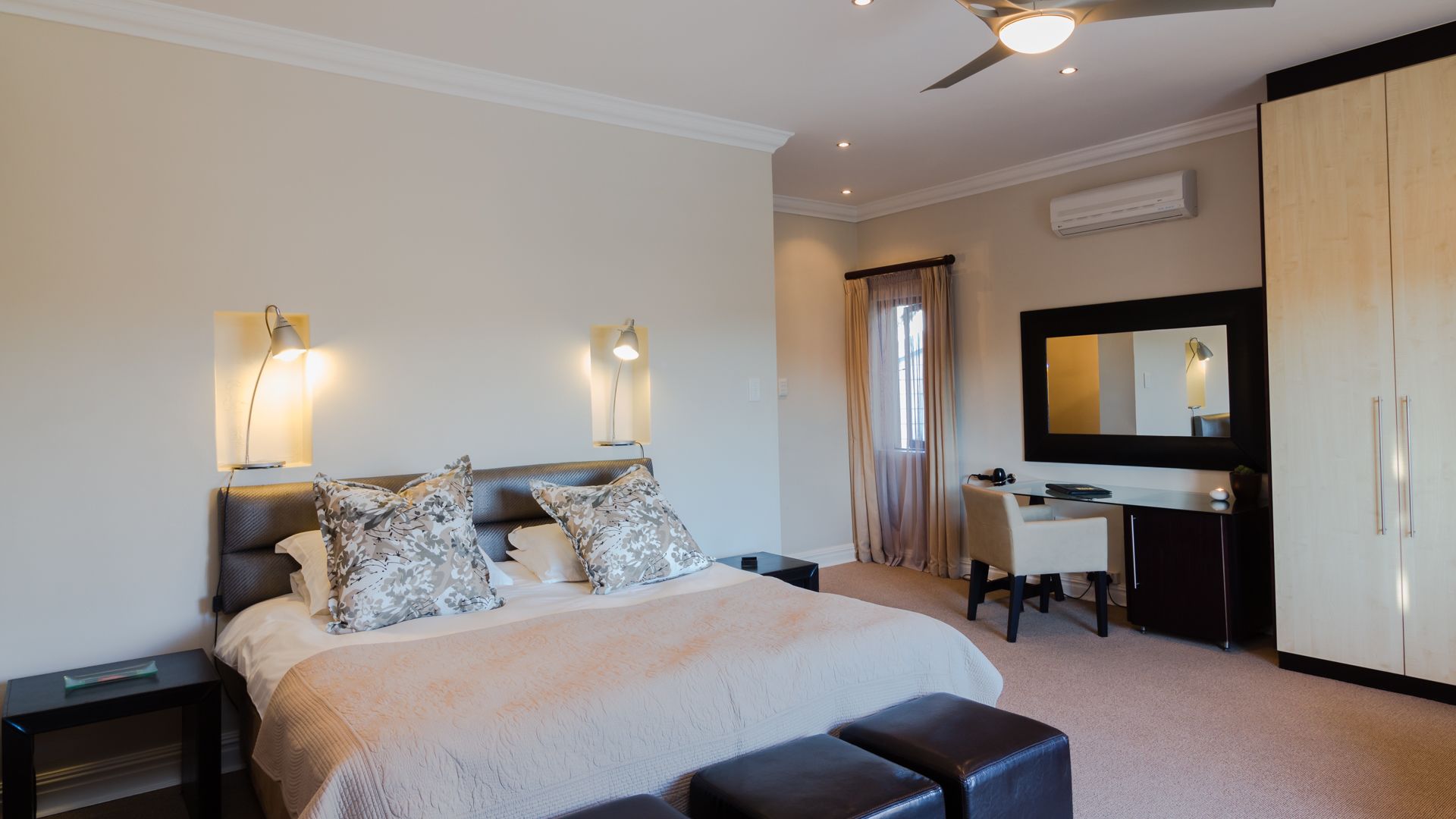 A modern bedroom with a bed, bedside tables, a desk, a chair, a wardrobe, and a ceiling fan.