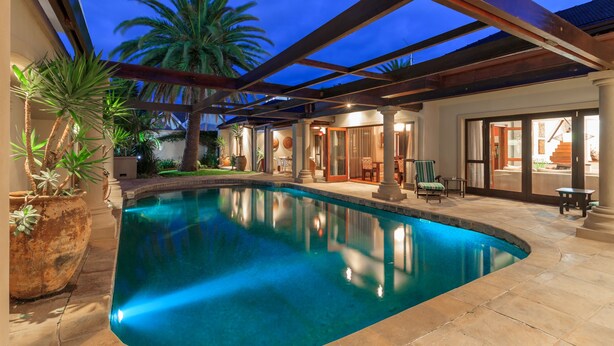 A swimming pool with a patio area, palm trees, and a covered seating area. - Manor 38 (Gqeberha (Port Elizabeth))