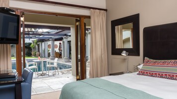 Habitación de hotel con cama, escritorio y vista al área de piscina exterior.