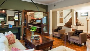 A spacious living room with a wooden coffee table, comfortable seating, a staircase, and a dining area with a view of the kitchen. - Manor 38 (Gqeberha (Port Elizabeth))