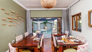 A dining area with a pool view, wooden furniture, and decorative fish wall art. - Manor 38 (Gqeberha (Port Elizabeth))