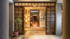 A hotel entrance with a wooden door, a potted plant, and a rug leading to a room with a bed and a desk. - Manor 38 (Gqeberha (Port Elizabeth))