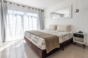 Ein modernes Schlafzimmer mit einem großen Bett, einem Nachttisch, einem Spiegel und transparenten Vorhängen.