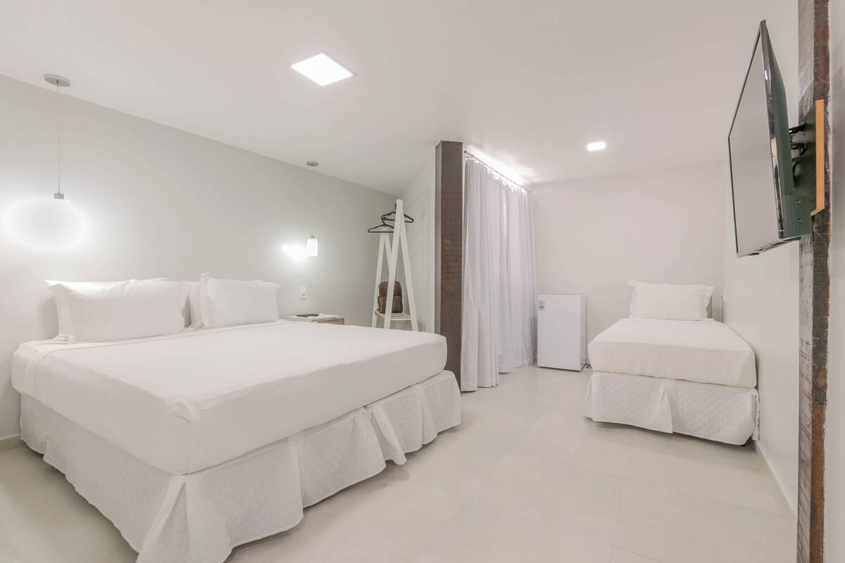 Une chambre d’hôtel avec deux lits, une armoire, un miroir et un téléviseur à écran plat fixé au mur.