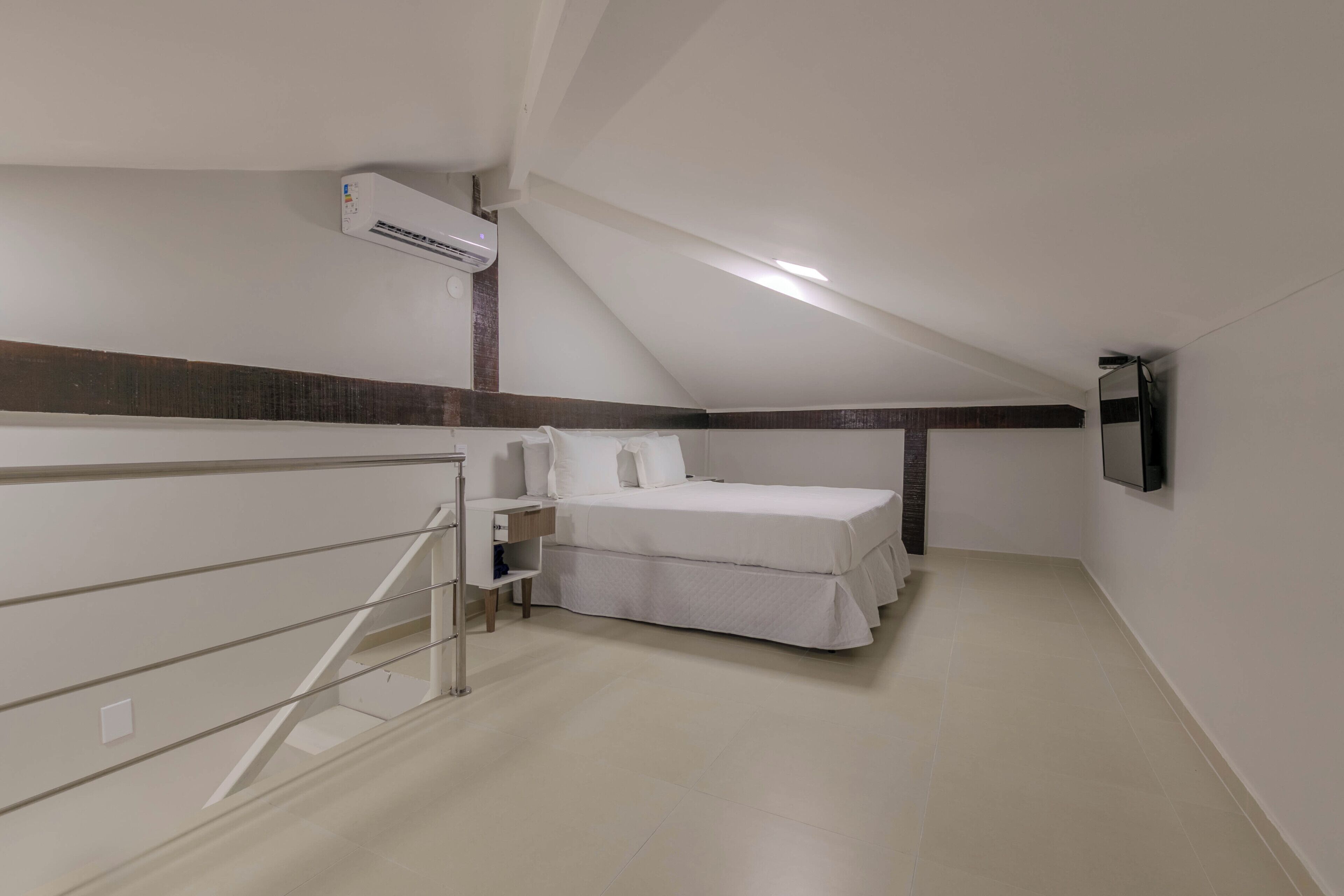 A bedroom with a bed, a TV mounted on the wall, and an air conditioning unit on the ceiling.