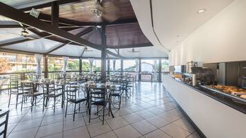 A spacious indoor dining area with multiple tables and chairs, a counter with food items, and a view of the outside.