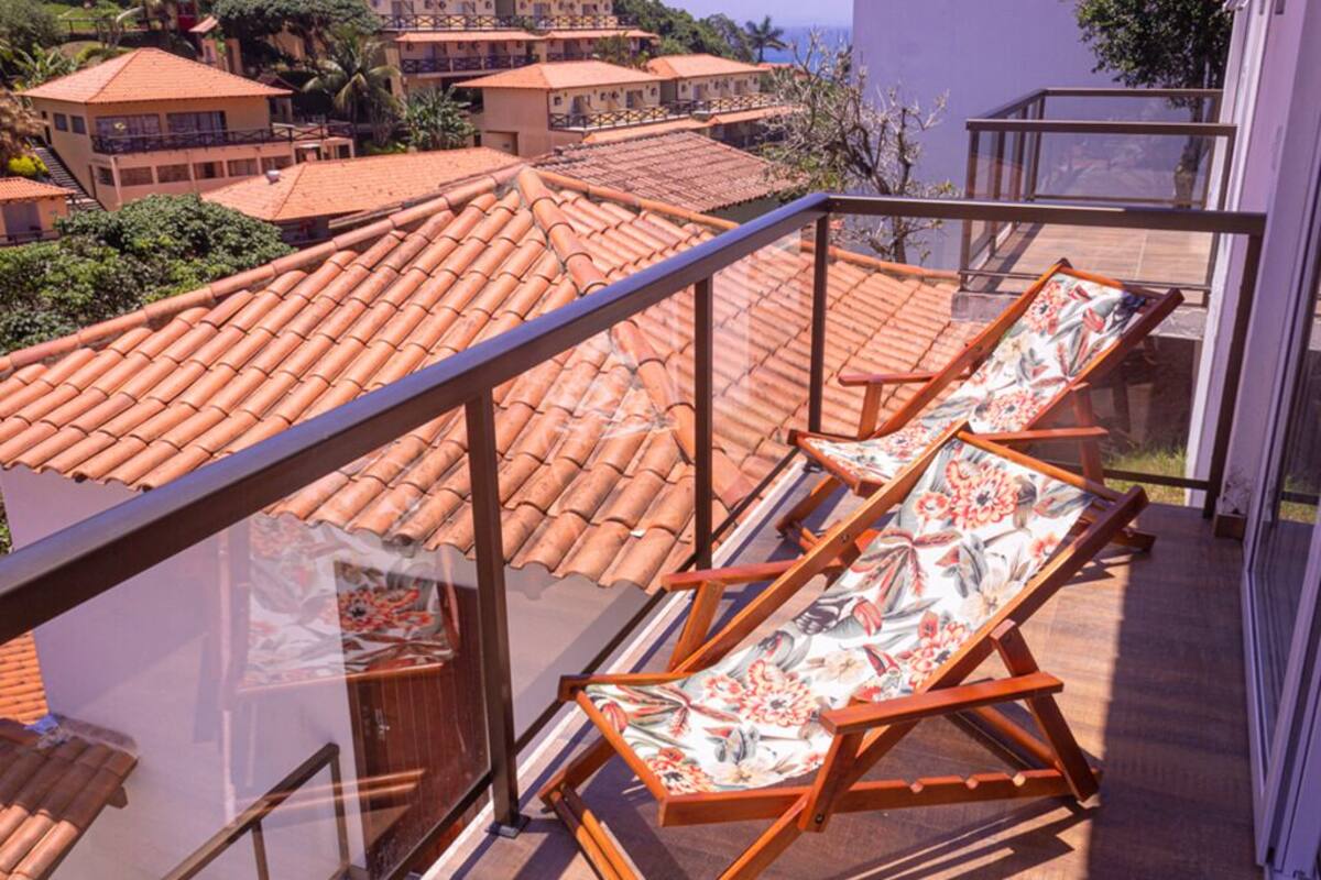 Un balcon doté de deux chaises longues et d’une balustrade en verre, donnant sur un quartier résidentiel aux toits de tuiles.