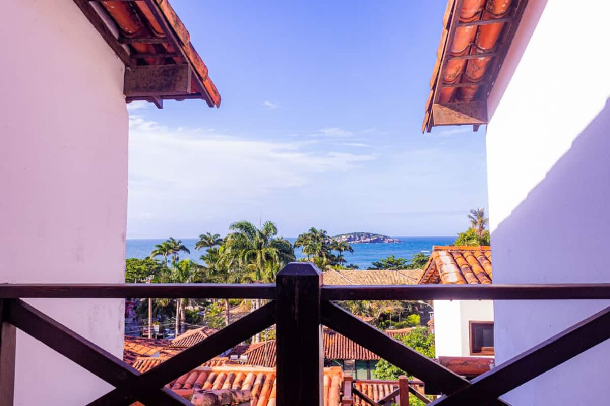 Un balcon avec vue sur la mer, des palmiers et des bâtiments aux toits recouverts de tuiles rouges.