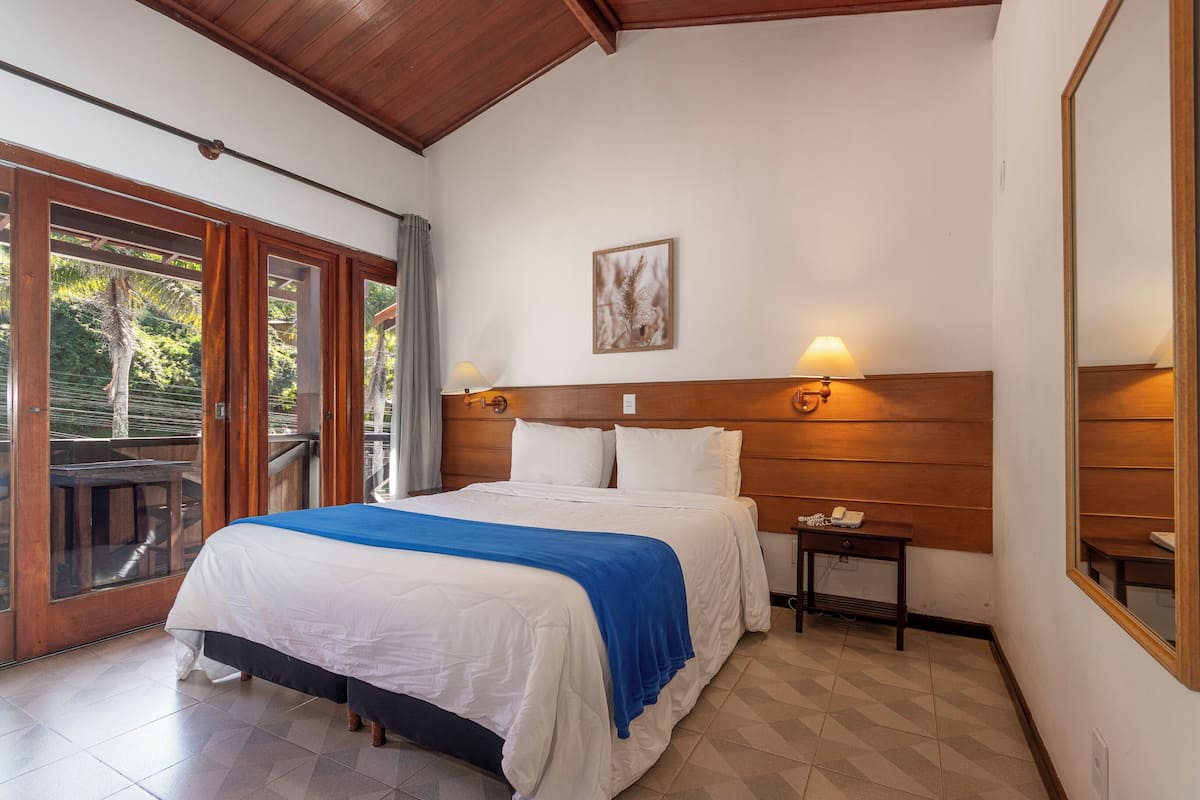 Une chambre à coucher comprenant un lit, une table de chevet, une lampe fixée au mur et une fenêtre donnant sur un paysage verdoyant.