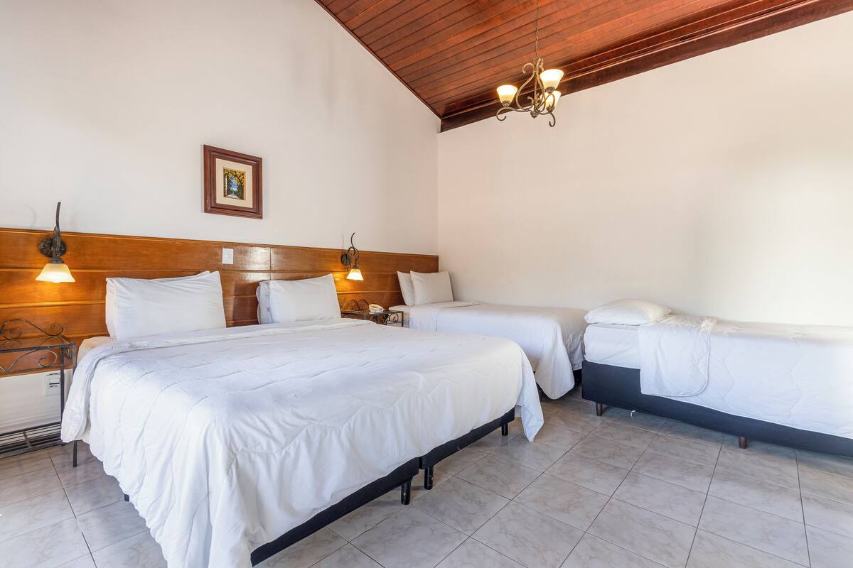 Une chambre d’hôtel avec deux lits, des têtes de lit en bois, un lustre et un tableau encadré au mur.