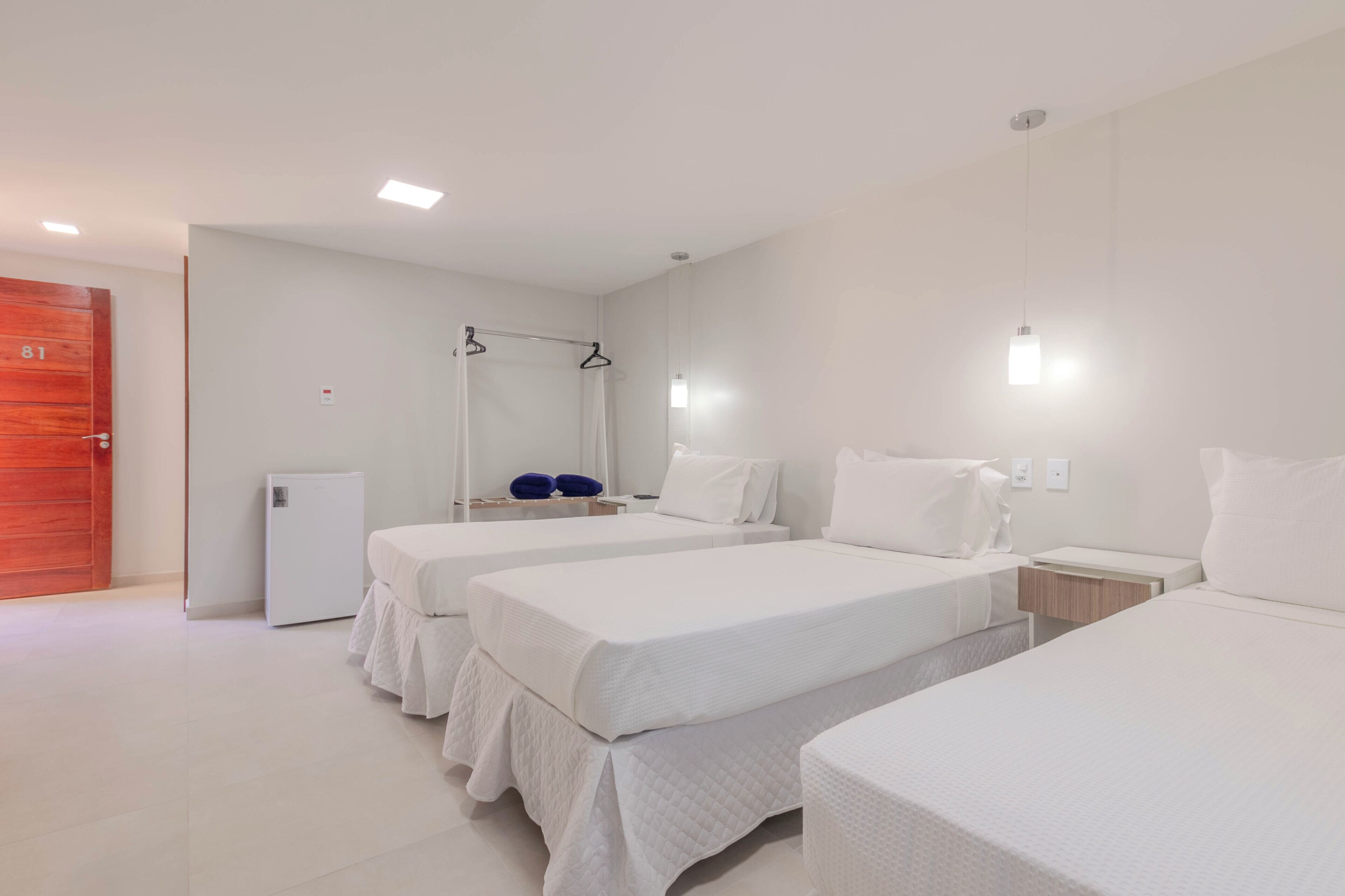 Ein Hotelzimmer mit drei Einzelbetten, einem kleinen Nachttisch, einem Spiegel und einem Kleiderschrank.