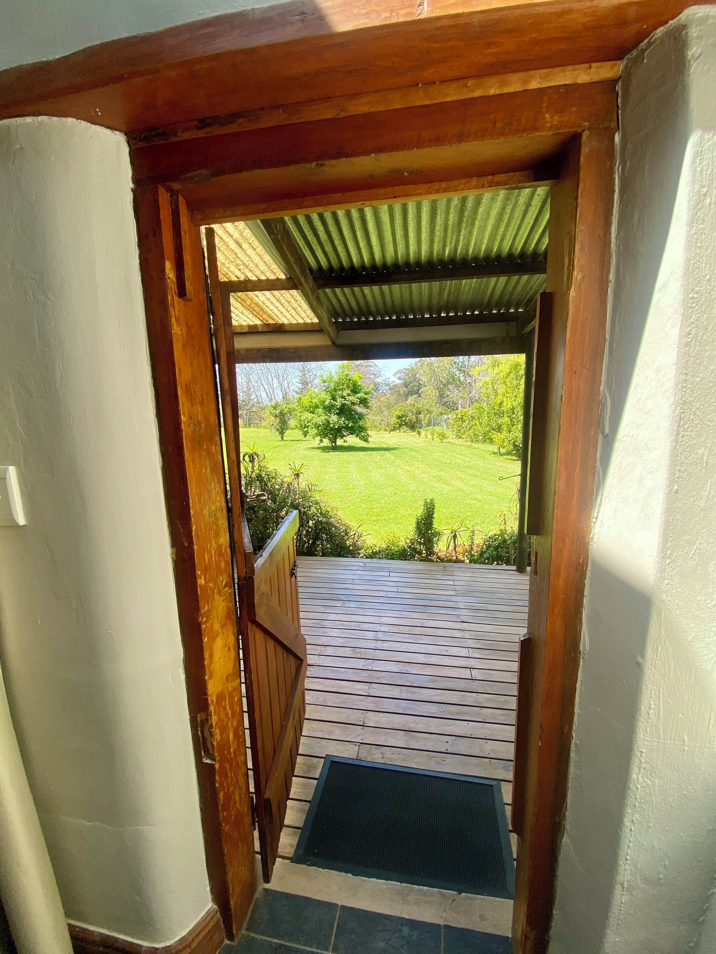 A wooden door leading to a covered outdoor area with a view of a green lawn and trees.