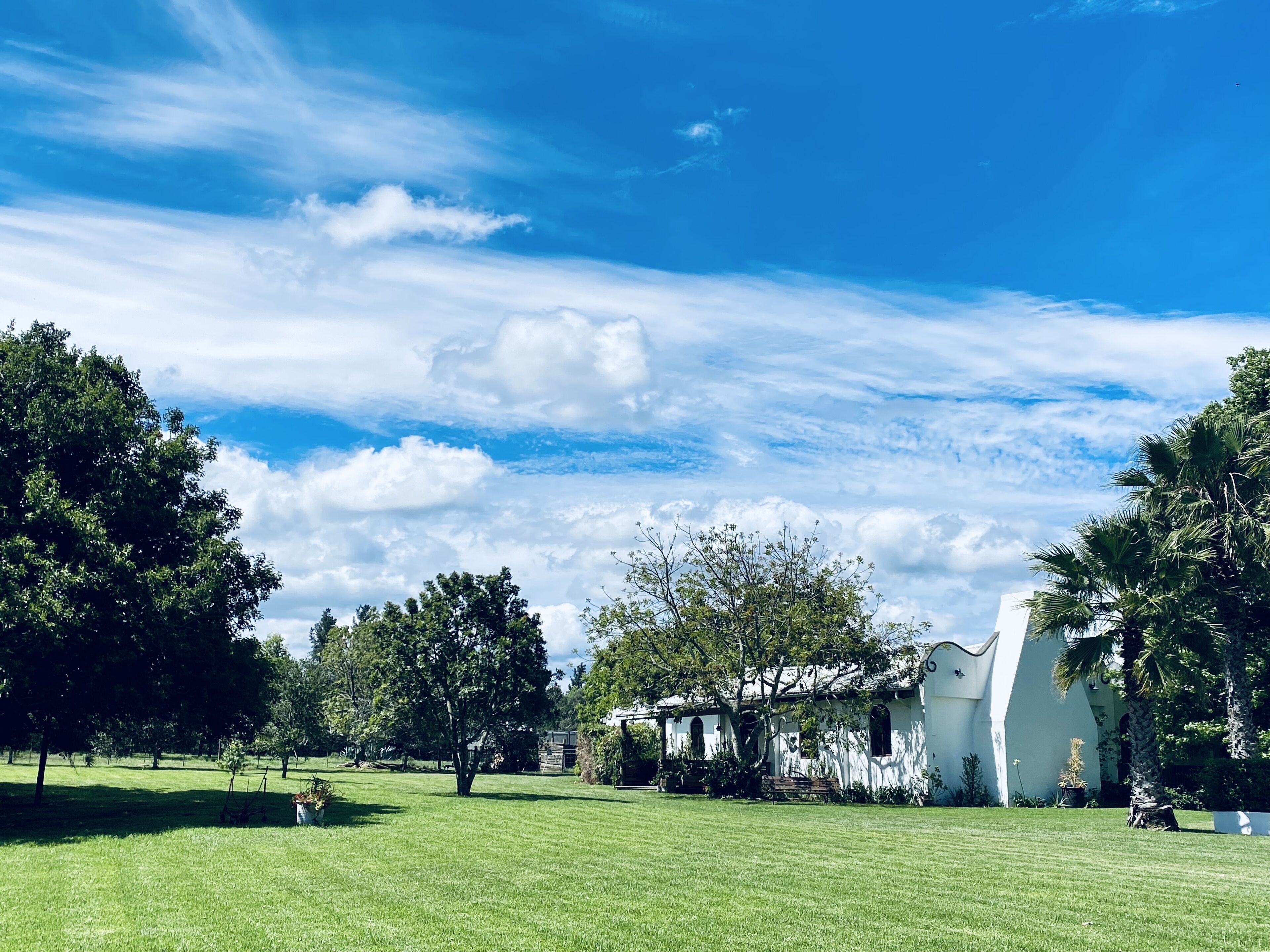 A white building with arched windows and a sloped roof, surrounded by green grass and trees.
