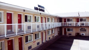 Un motel à plusieurs étages, avec des chambres numérotées, un parking et un espace extérieur abrité avec des sièges.