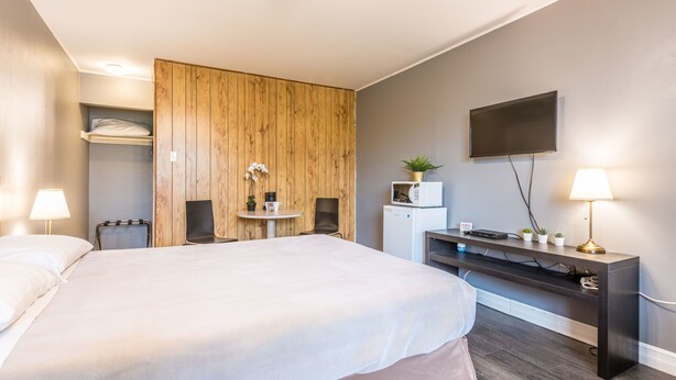 Une chambre d’hôtel avec un grand lit, une cloison en bois, un téléviseur fixé au mur, un bureau avec une lampe et un petit réfrigérateur.