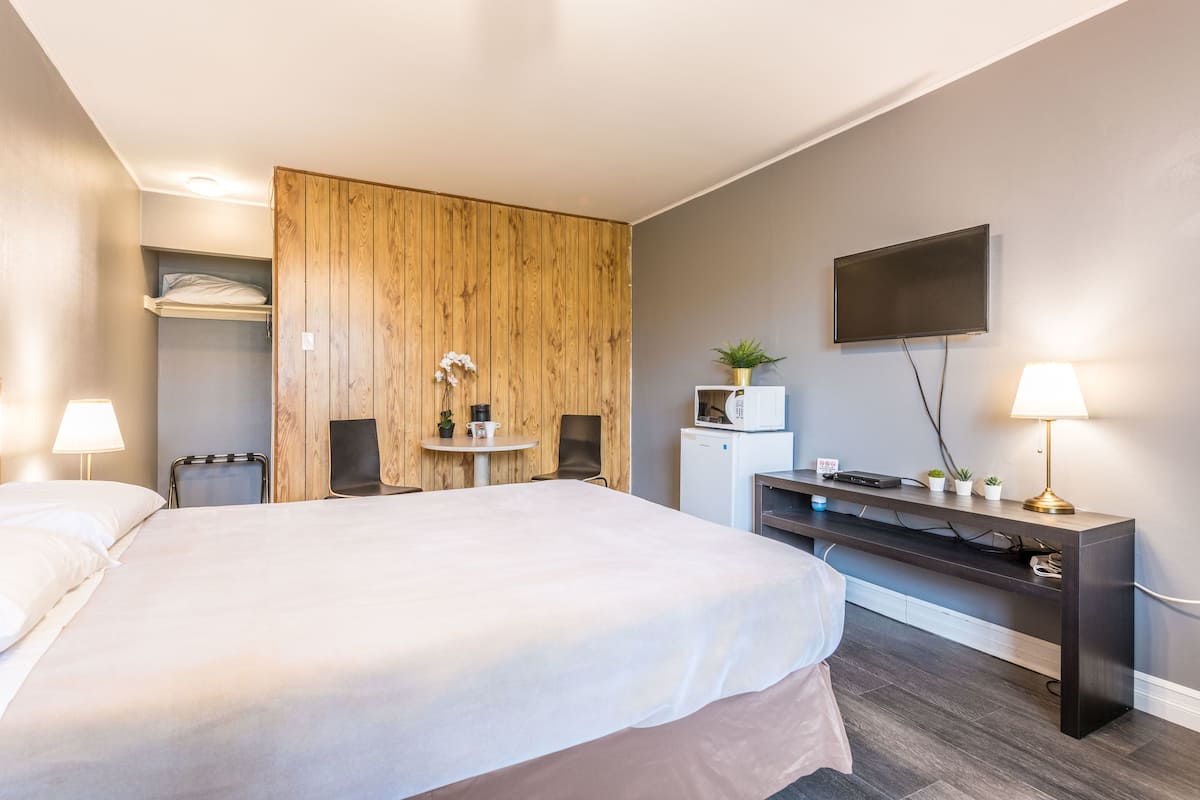 Ein Hotelzimmer mit einem großen Bett, einer Holzwand, einem an der Wand montierten Fernseher, einem Schreibtisch mit Lampe und einem kleinen Kühlschrank.