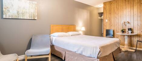 A modern bedroom with a bed, a chair, a bedside table, and a wall-mounted artwork.