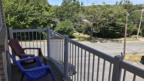 Un balcon avec deux fauteuils Adirondack, une balustrade blanche et une vue sur un parking et des arbres.