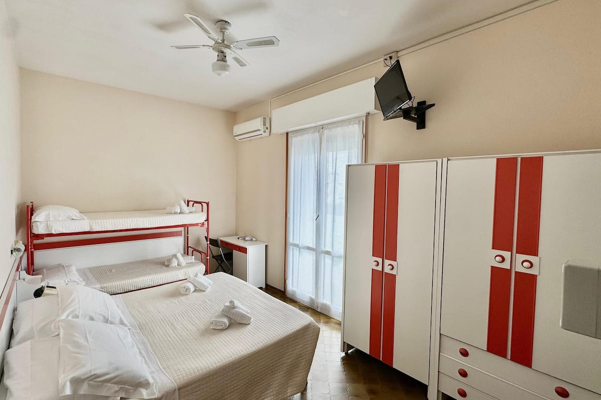 Une chambre d’hôtel équipée d’un lit superposé, d’un bureau, d’une armoire et d’un ventilateur de plafond.