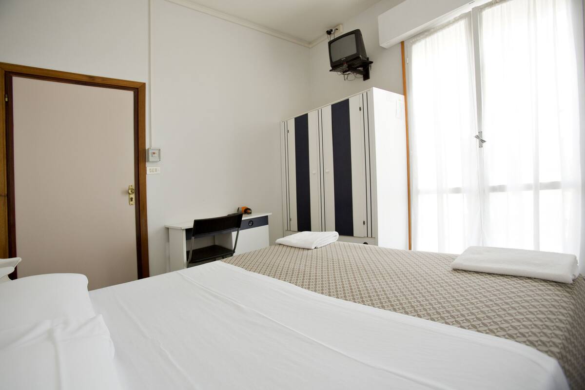 Une chambre d’hôtel avec deux lits, un bureau, une armoire et un téléviseur.