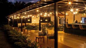 An outdoor dining area with multiple tables and chairs, a bar area, and a covered seating section. - Natural Lodge Caño Negro (Caño Negro)