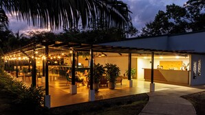 An outdoor dining area with tables and chairs, surrounded by potted plants and a pathway leading to a building. - Natural Lodge Caño Negro (Caño Negro)
