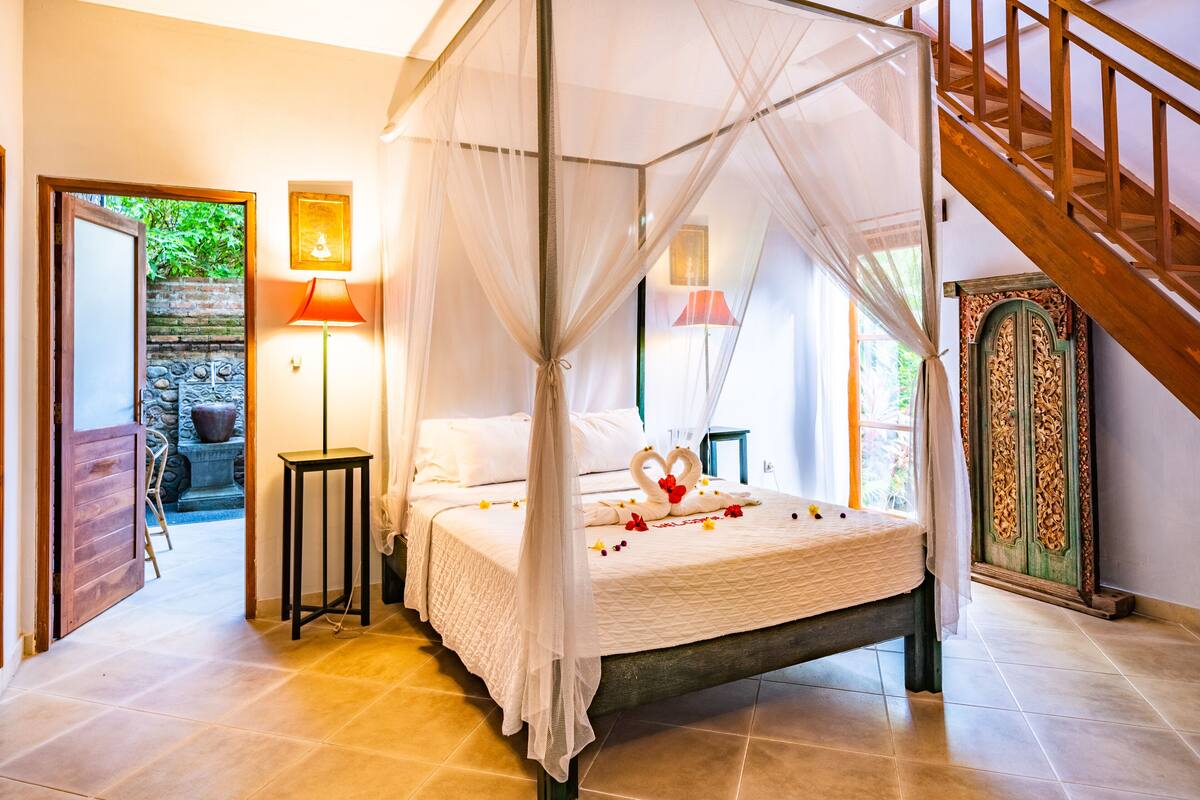 A four-poster bed with a canopy, a wooden staircase, and a view of a garden through an open door.