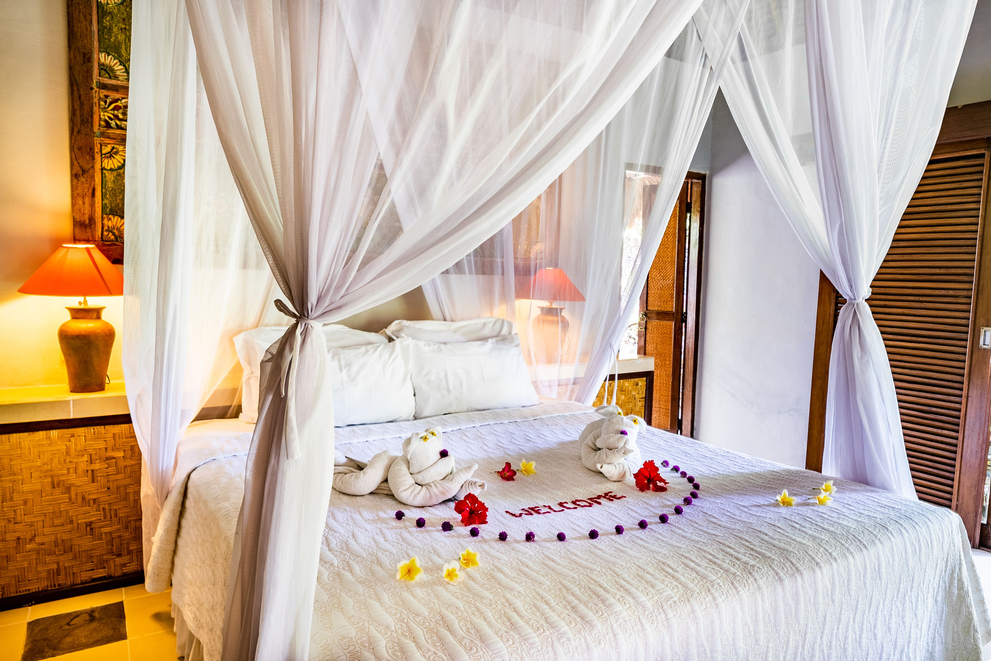A bed with a canopy, white linens, and a welcome mat with flowers.