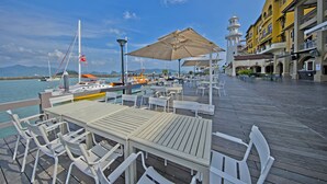 A waterfront deck with tables and chairs, a lighthouse, and a building with balconies. - Resorts World Langkawi (Langkawi)