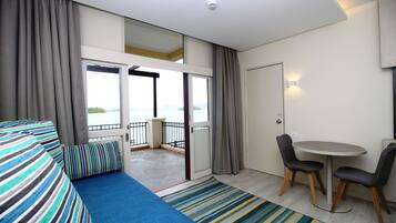 A hotel room with a balcony, a sofa, a dining table with chairs, and a view of the sea.