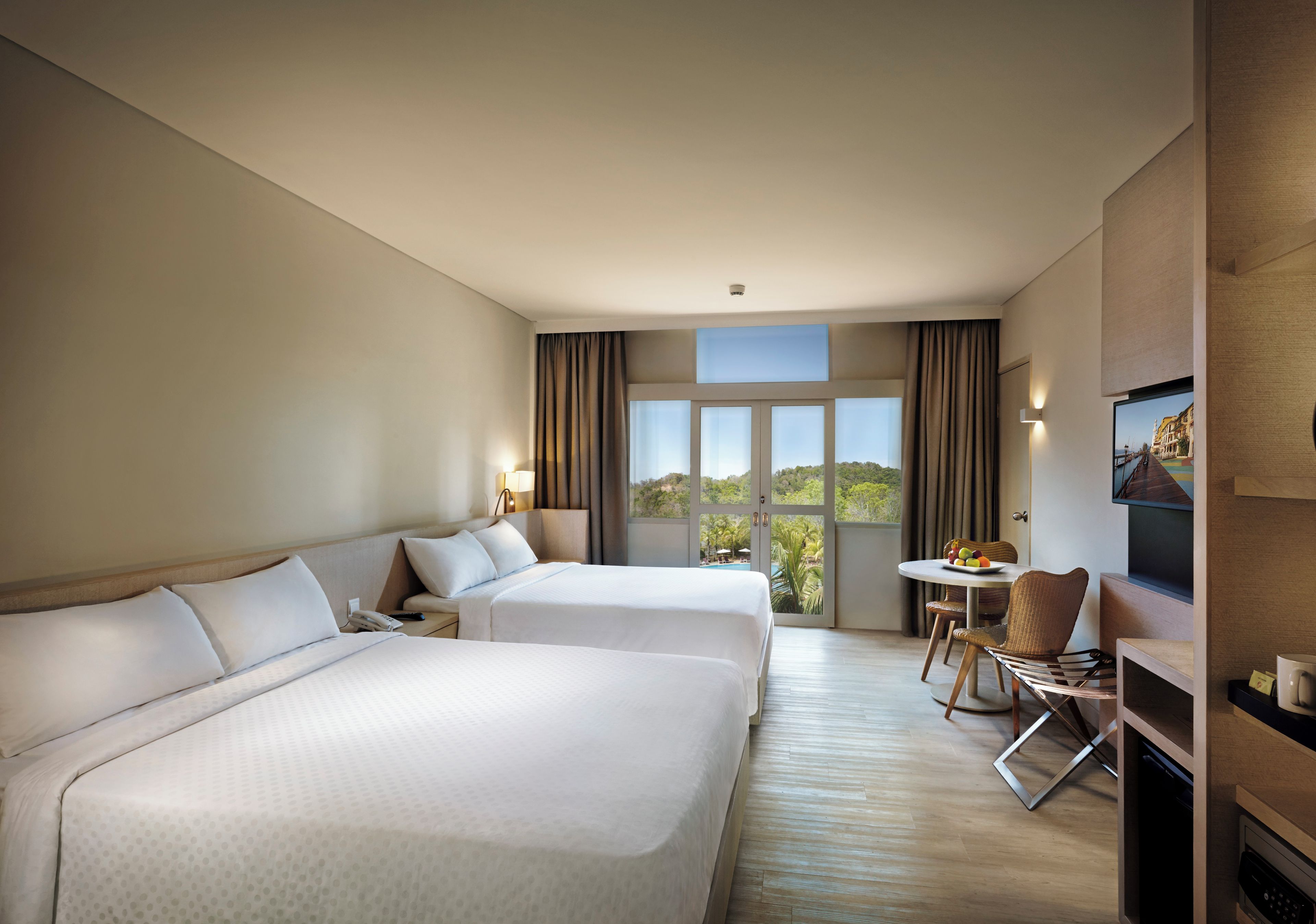 A hotel room with two beds, a dining table with chairs, a television, and a view of the outdoors.
