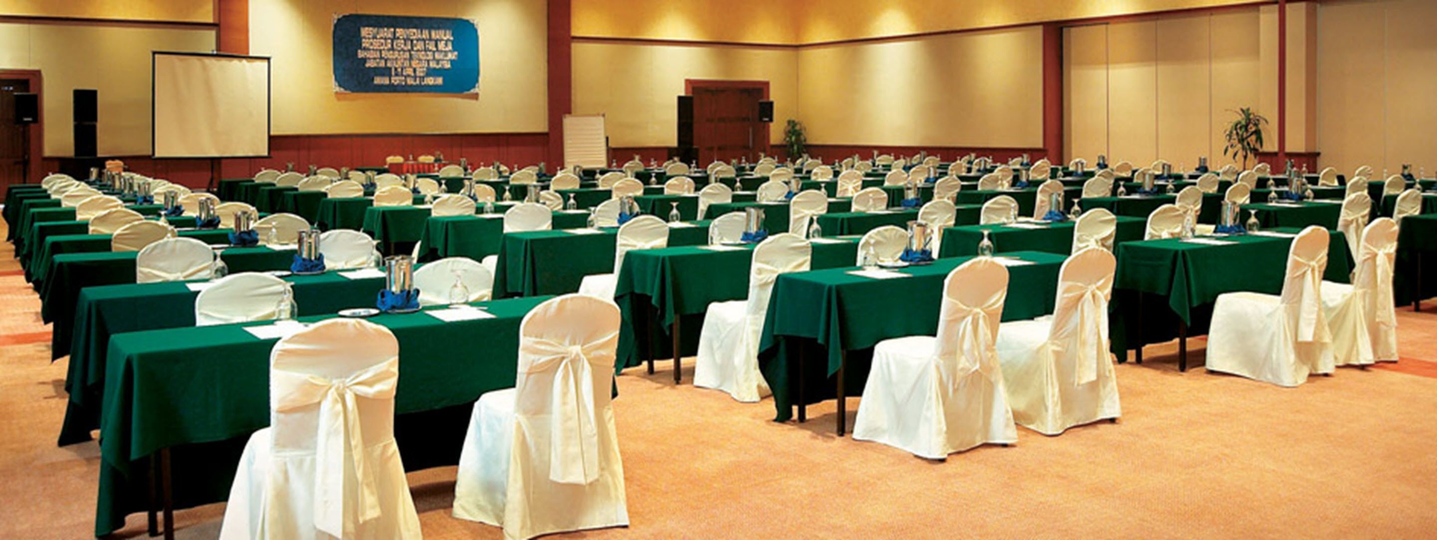 A conference room with rows of tables, chairs, and a projector screen.