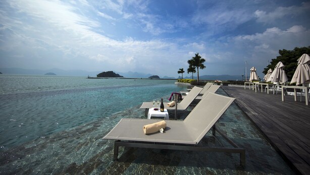 A serene waterfront resort with clear blue waters, lounge chairs, and umbrellas. - Resorts World Langkawi (Langkawi)