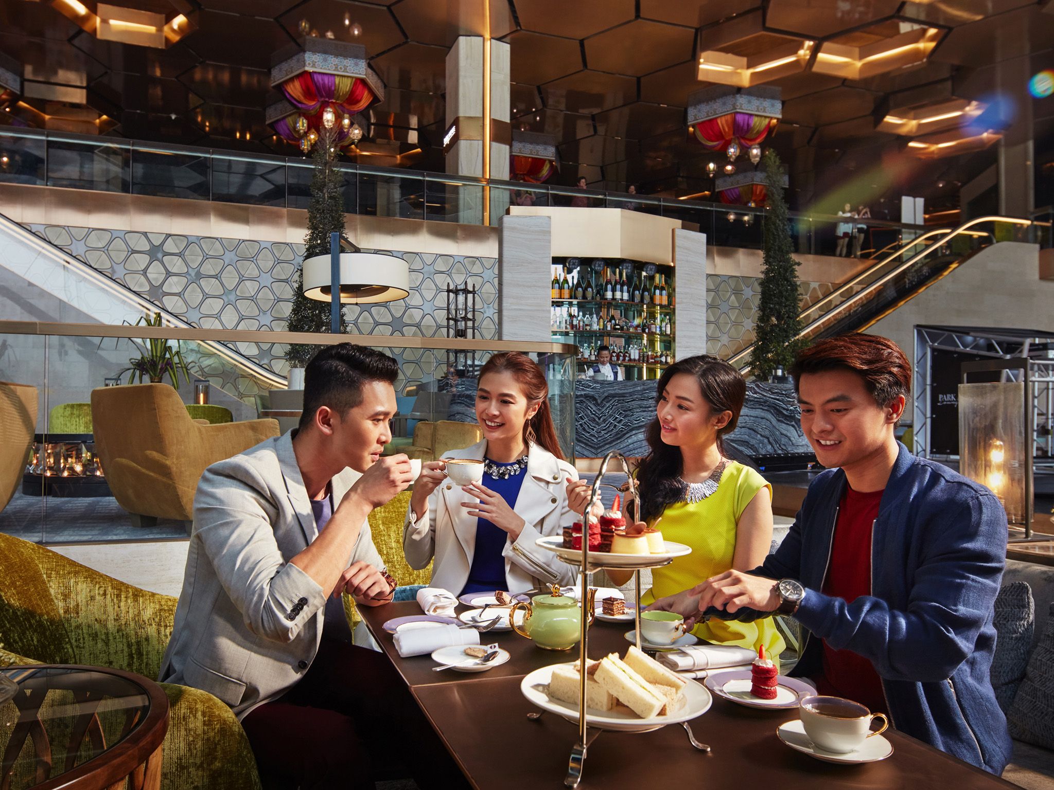 A group of people dining at a table in a modern indoor setting with a bar and staircase in the background.