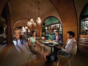 A restaurant with a high arched ceiling, hanging pendant lights, and a bar area with bottles and glasses. - Resorts World Genting - Genting Grand (Genting Highlands)
