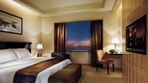 A hotel room with a large bed, a desk with a lamp, a chair, a TV, and a window with curtains. - Resorts World Genting - Genting Grand (Genting Highlands)