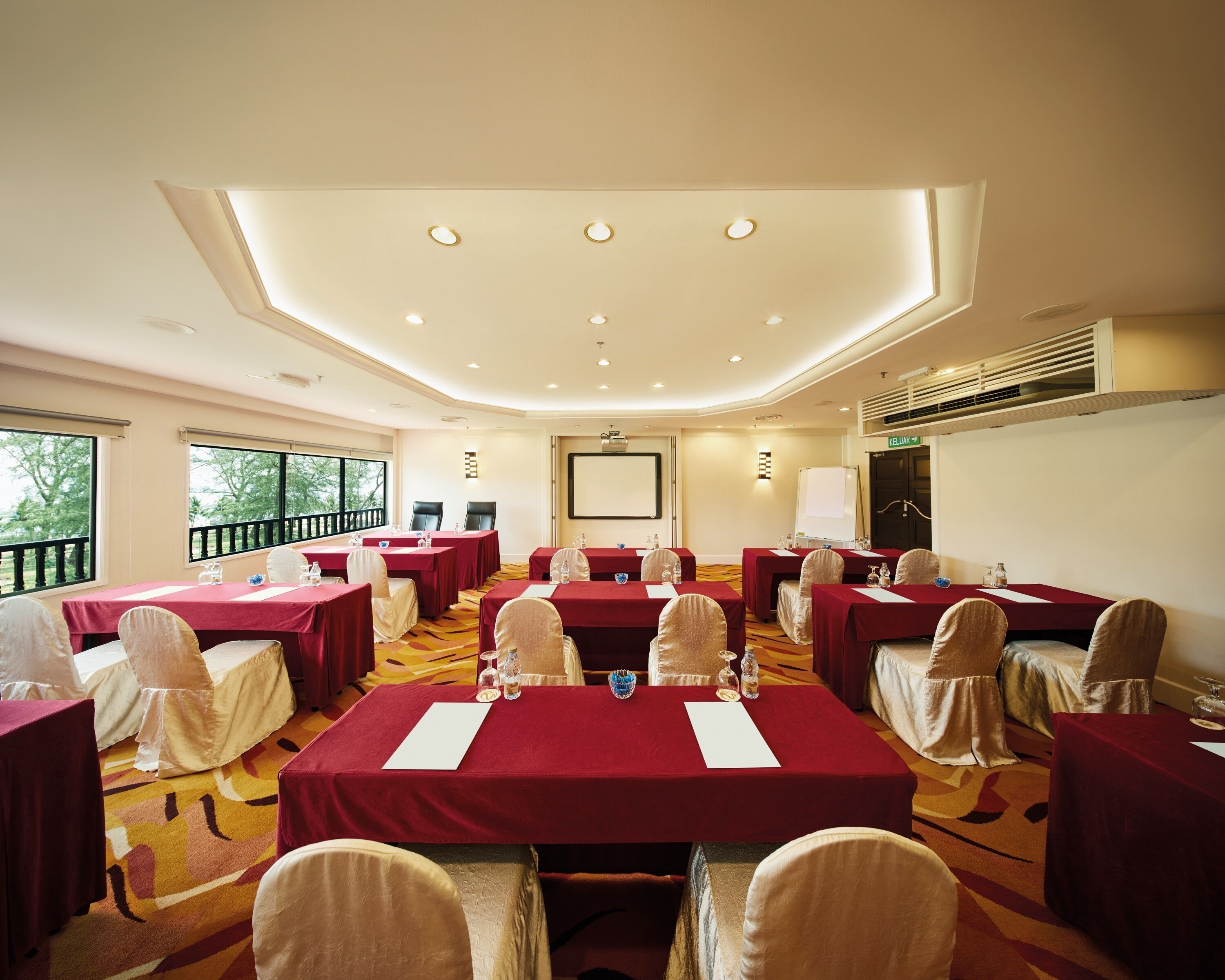 A conference room with multiple tables, chairs, and a large screen.