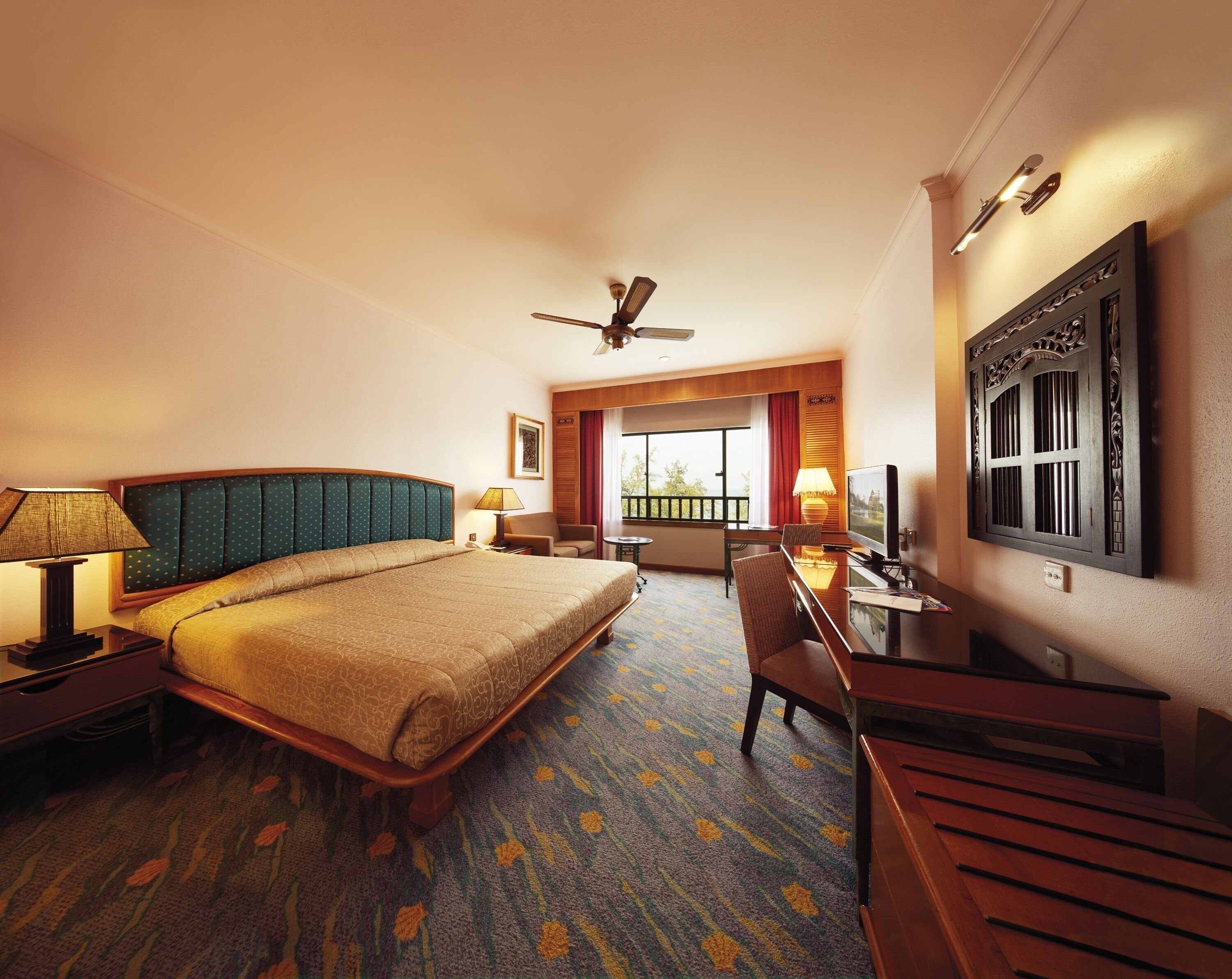 A hotel room with a large bed, a desk with a chair, a television, and a ceiling fan.
