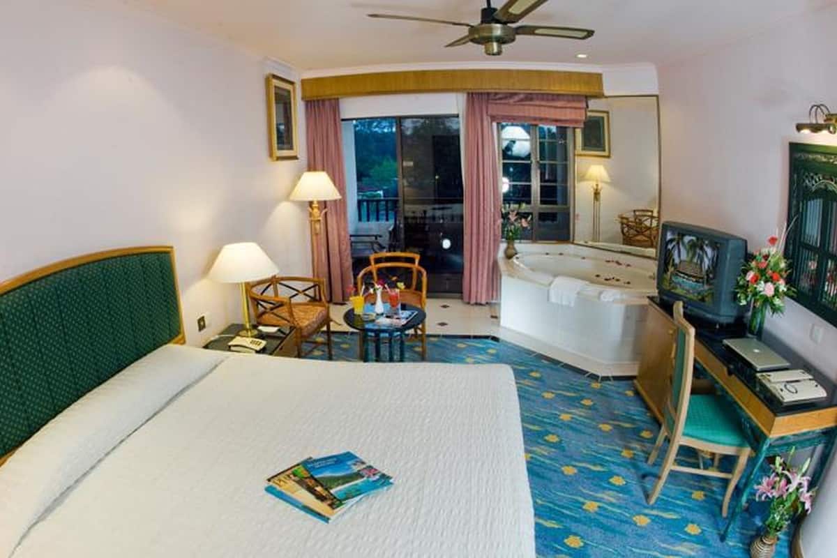 A hotel room with a bed, a desk with a computer, a TV, a chair, a small table with drinks, and a balcony with a view.