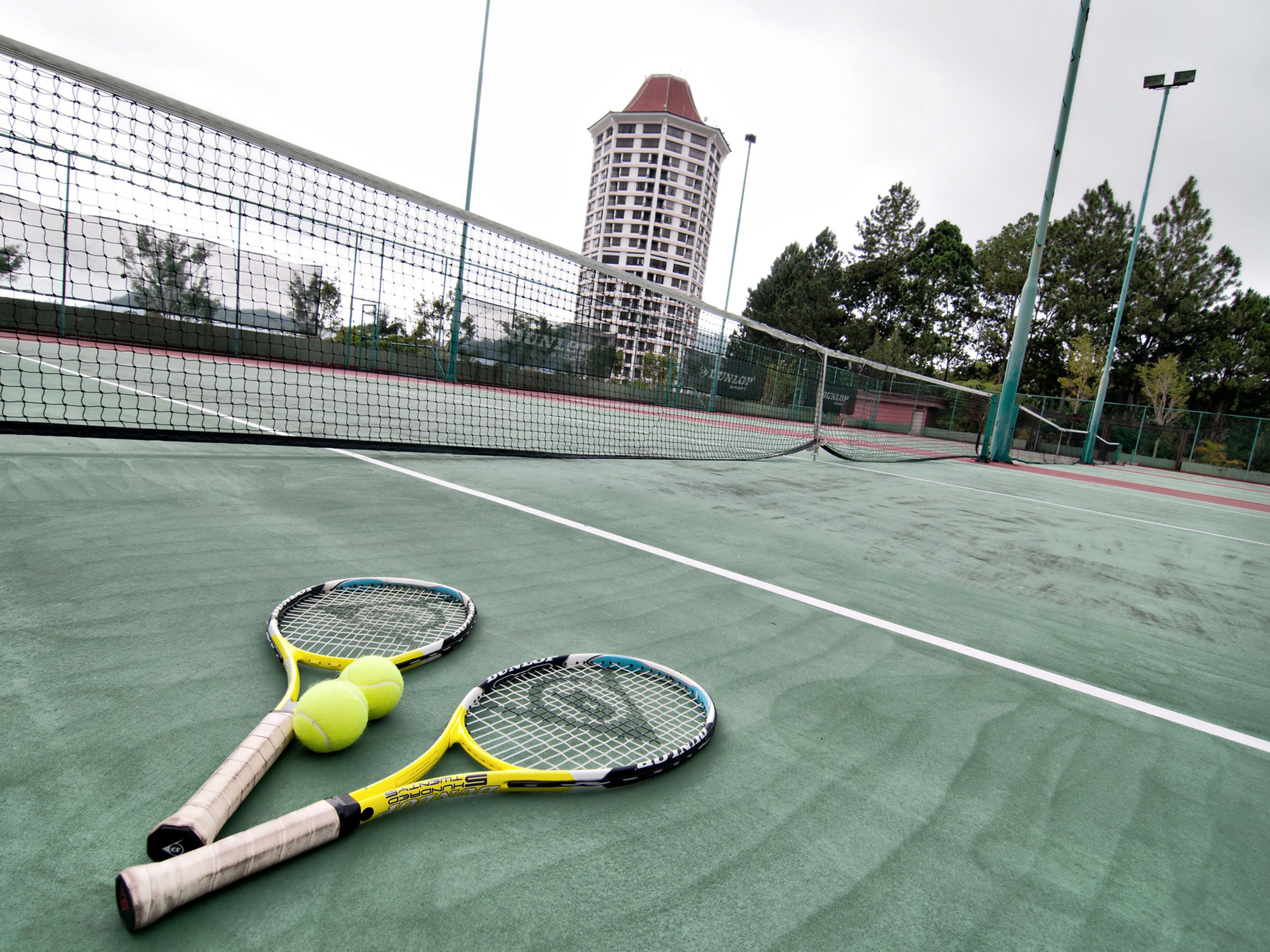A tennis court with two tennis rackets and three tennis balls.