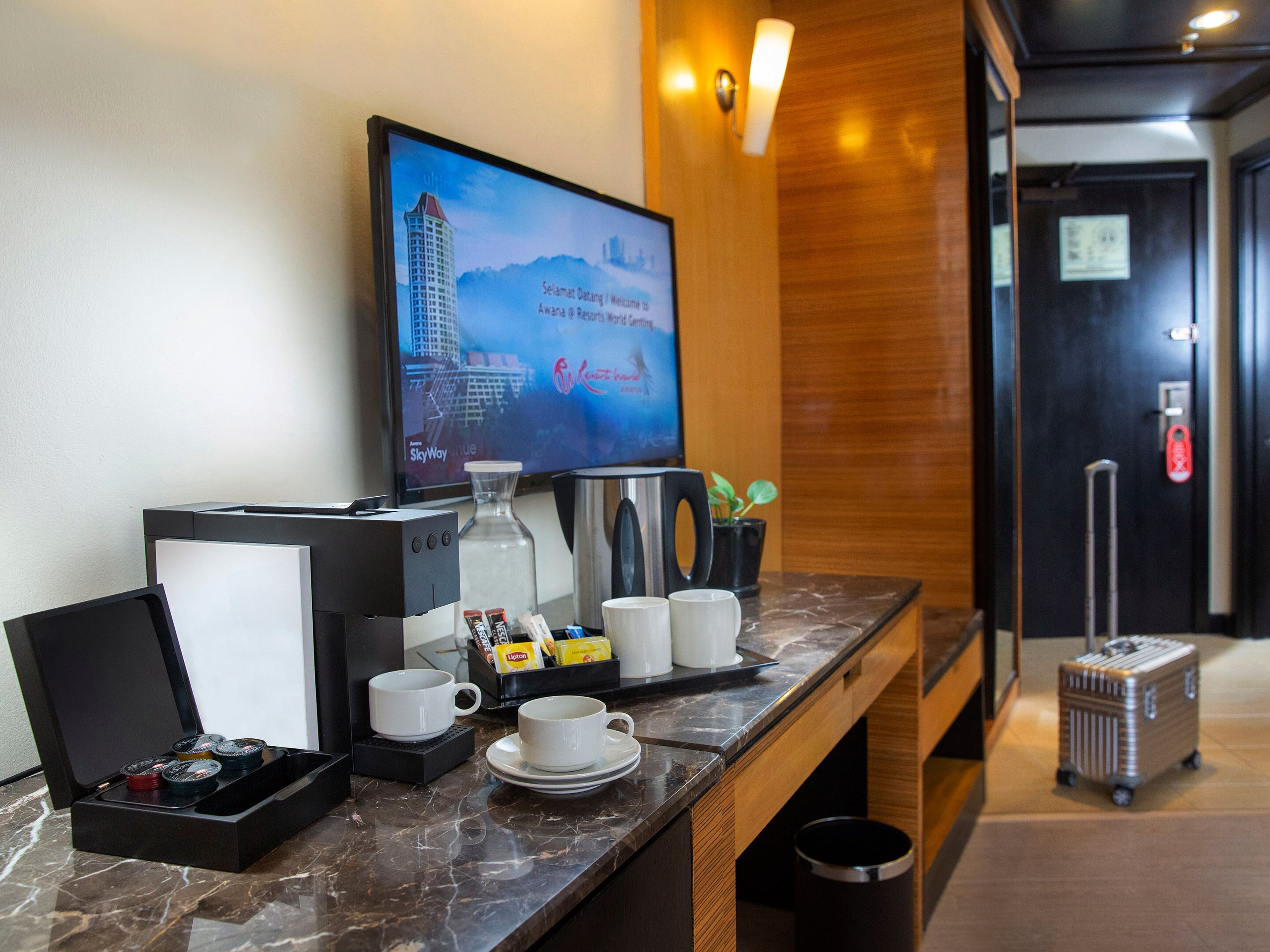 A hotel reception area with a coffee machine, tea kettle, and a television displaying a cityscape.