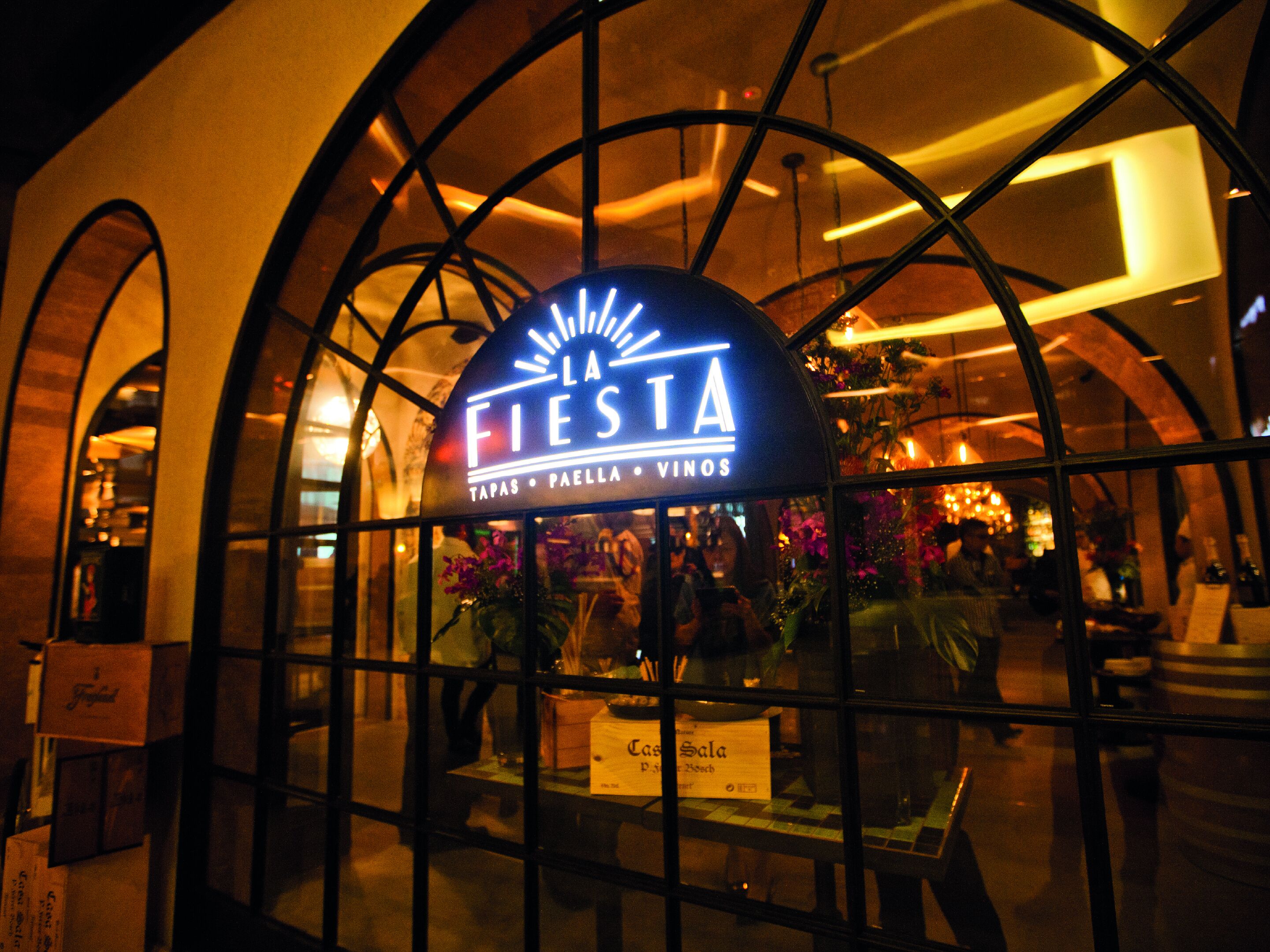 Une enseigne de restaurant portant le nom « La Fiesta » et affichant au menu des tapas, une paella et une sélection de vins.