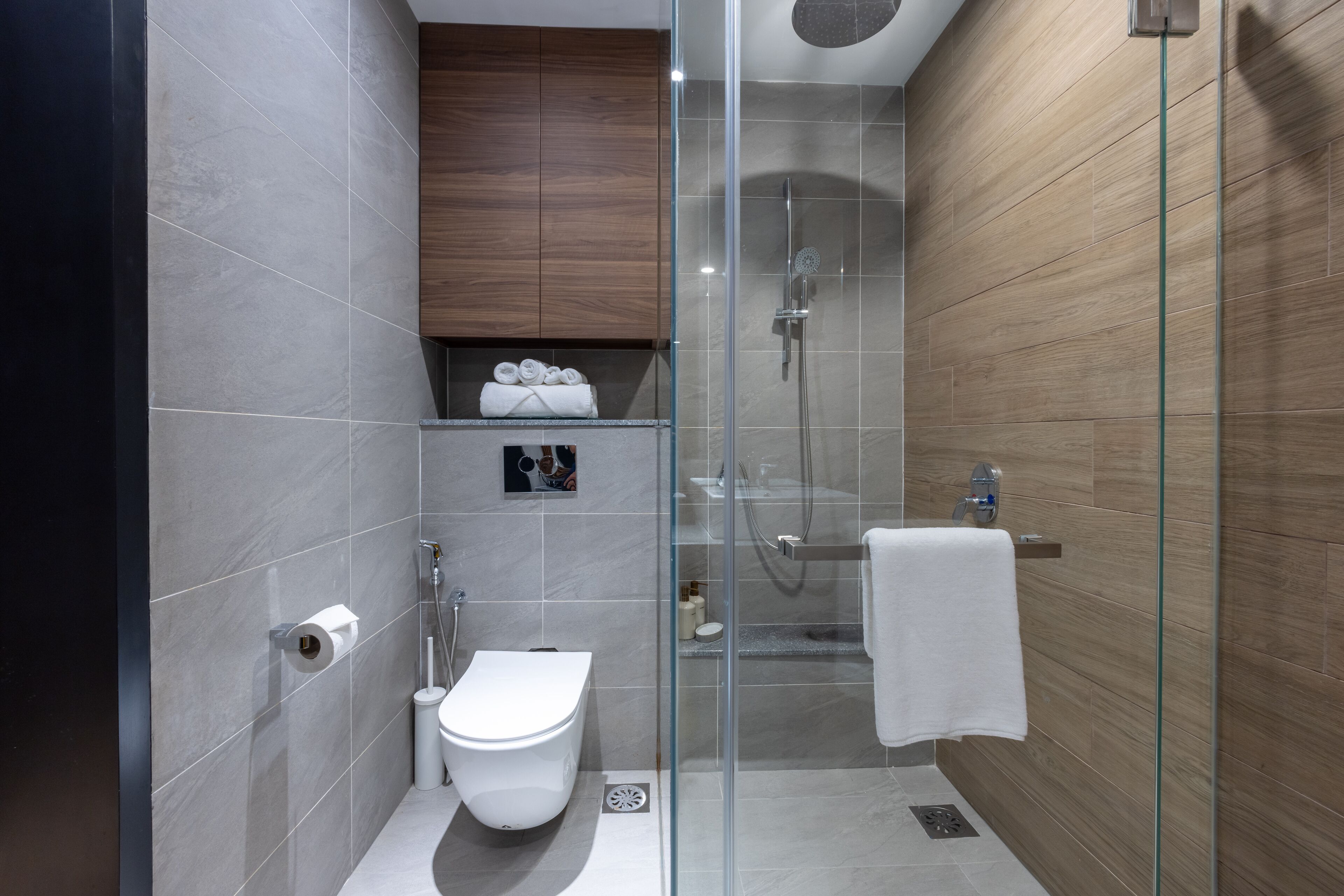 A modern bathroom with a glass-enclosed shower, a toilet, and a towel rack.