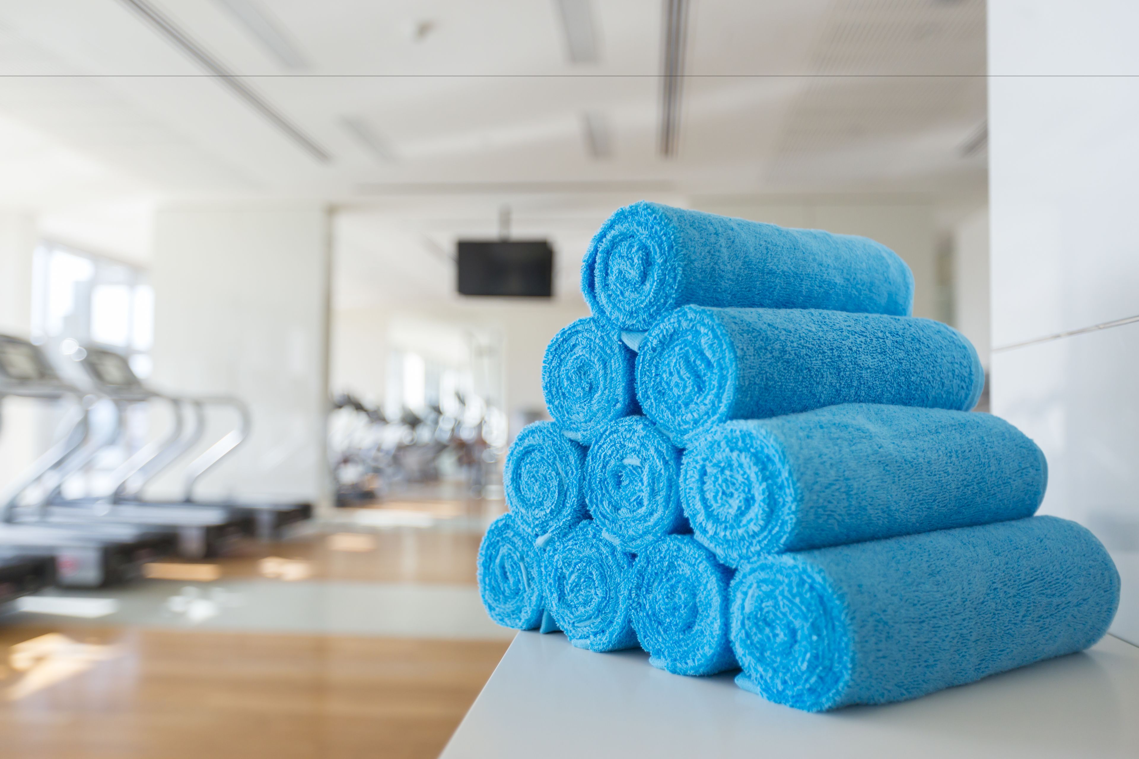 A stack of blue towels in a gym with exercise equipment in the background.