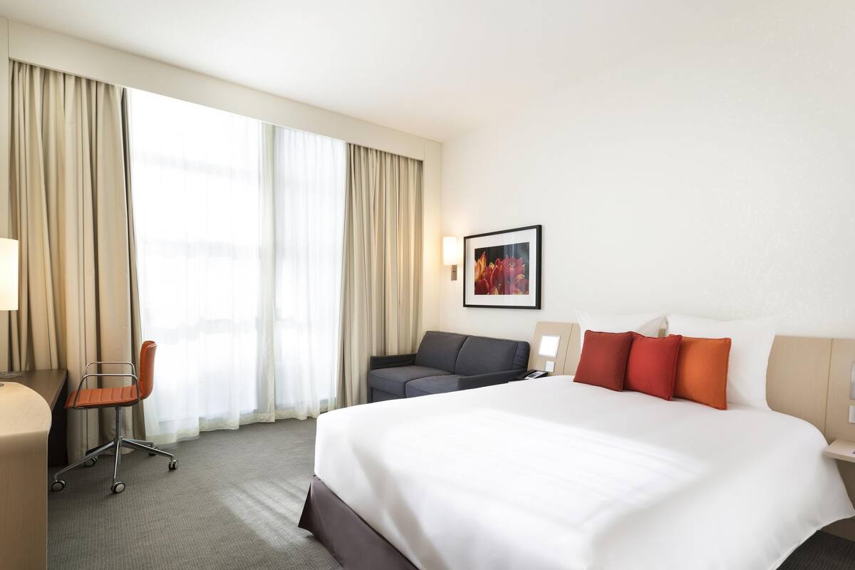 Een hotelkamer met een groot bed, een bureau met stoel, een bank en een schilderij aan de muur.